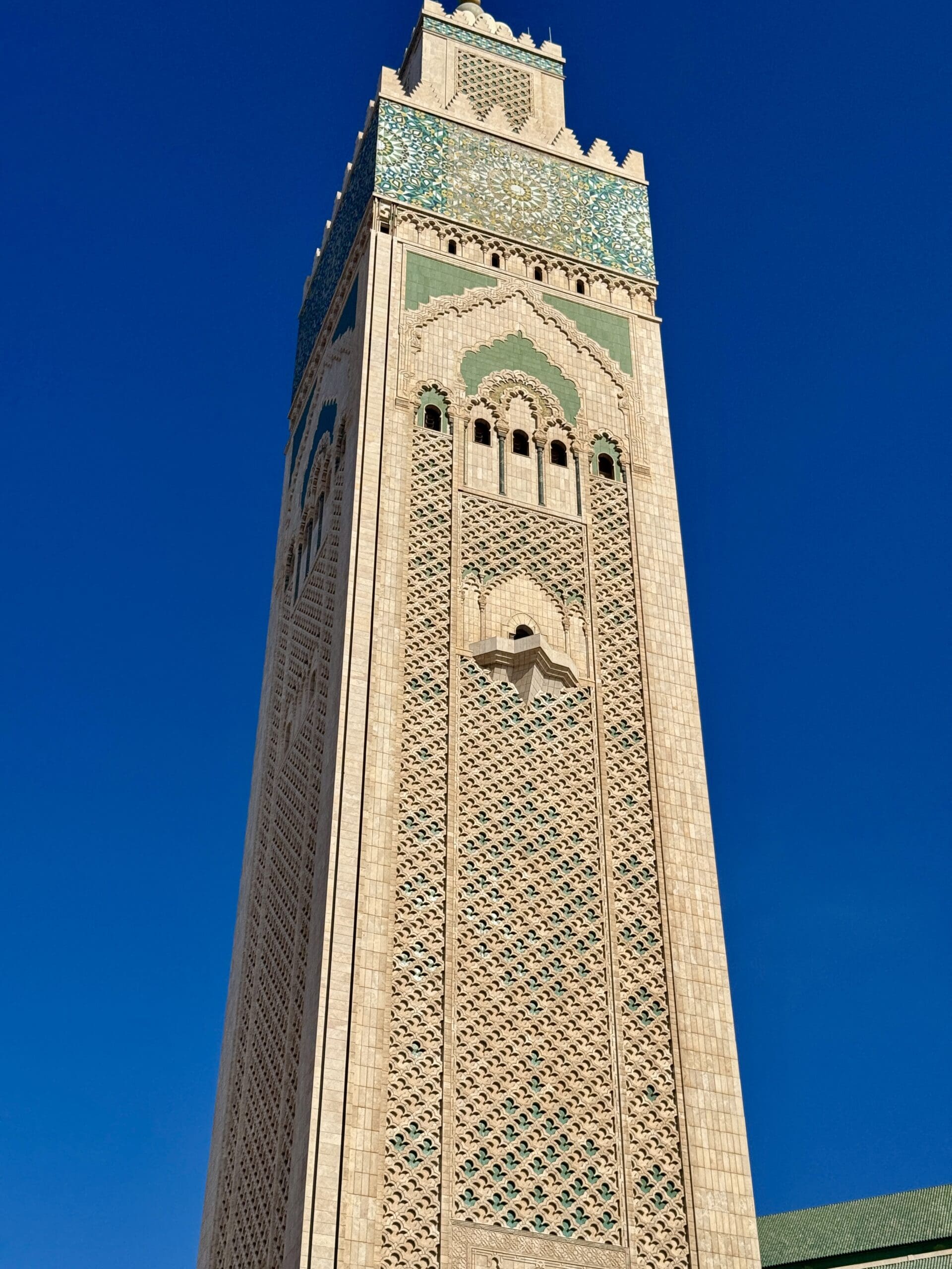 The Hassan II Mosque minaret in Casablanca, Morocco, showcasing intricate zellige tilework and geometric carvings against a vivid blue sky.